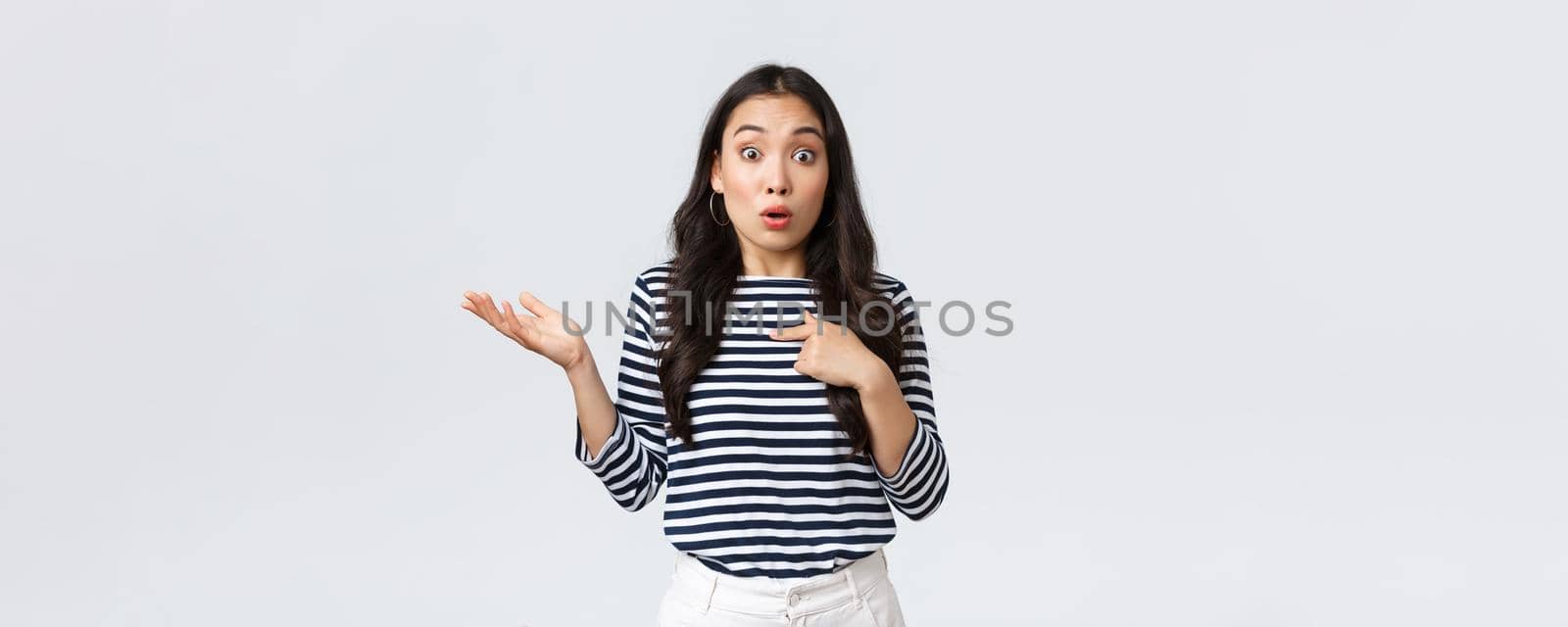 Lifestyle, beauty and fashion, people emotions concept. Shocked and surprised girl pointing at herself and shrugging as was picked or chosen, standing white background.