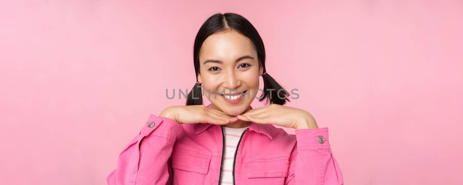 Skin care and cosmetology concept. Beautiful asian girl smiling and laughing, showing clean healthy facial skin, posing against pink background. Copy space