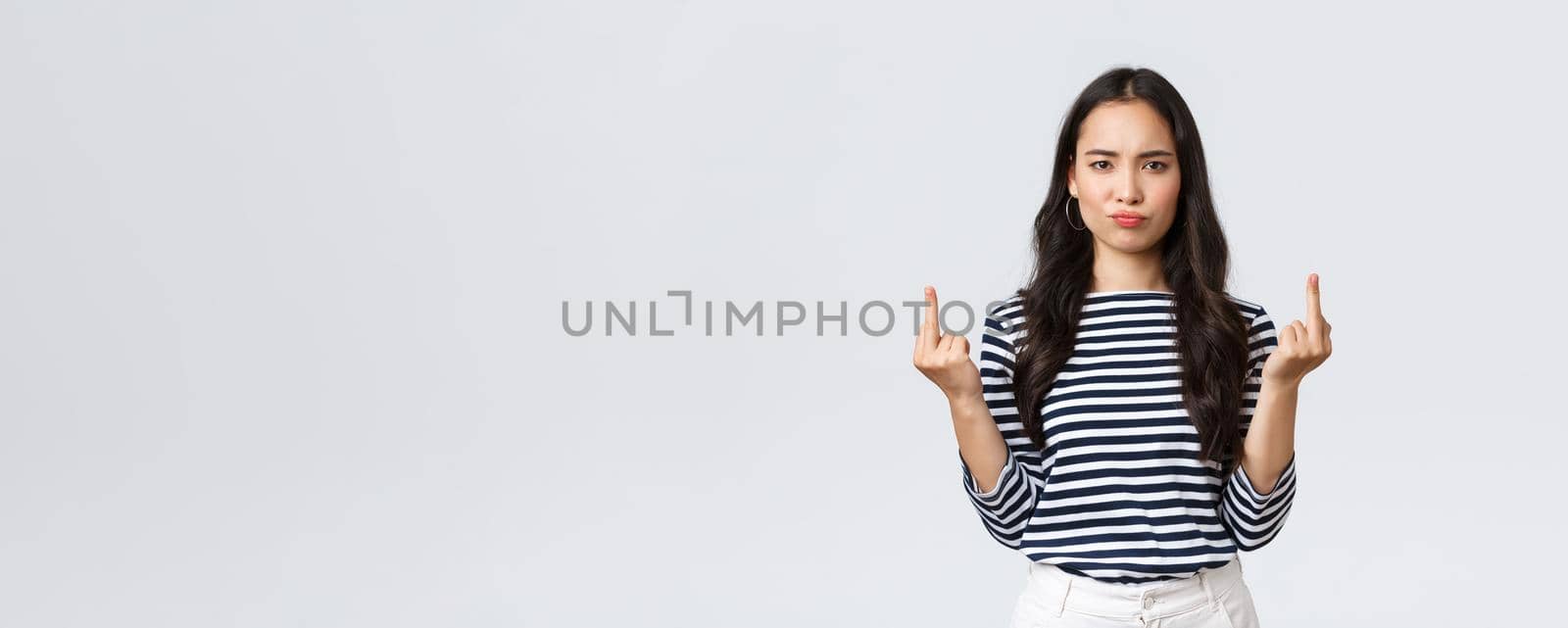 Lifestyle, beauty and fashion, people emotions concept. Pouting bothered young pissed-off asian female look annoyed and showing middle-fingers rude gesture, white background.