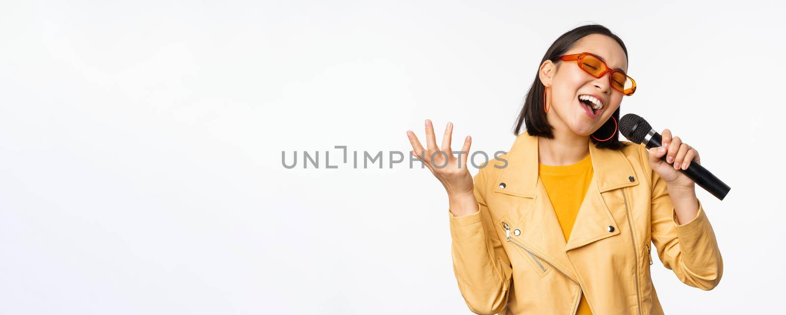 Singing girl holding microphone, performing songs at karaoke, standing over white background. Copy space