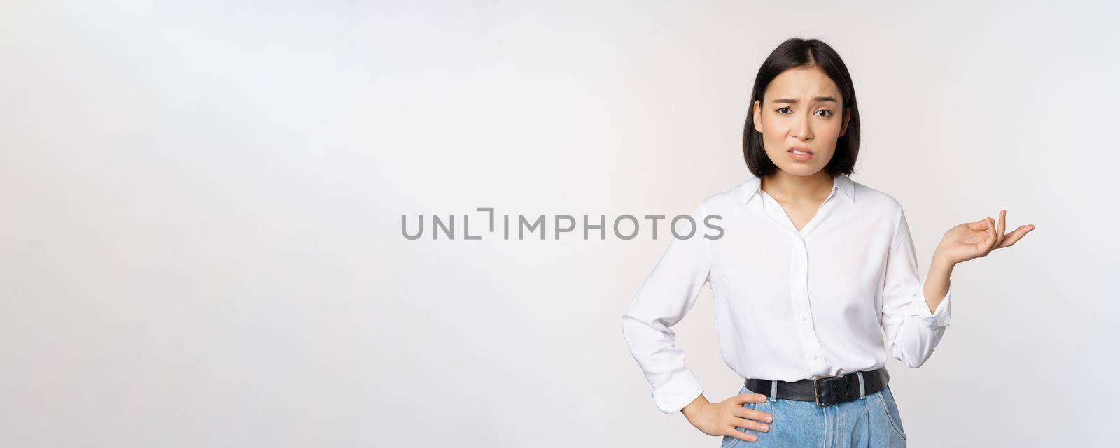 Portrait of confused asian woman asking so what, whats your problem gesture, staring puzzled, clueless and annoyed, standing over white background.