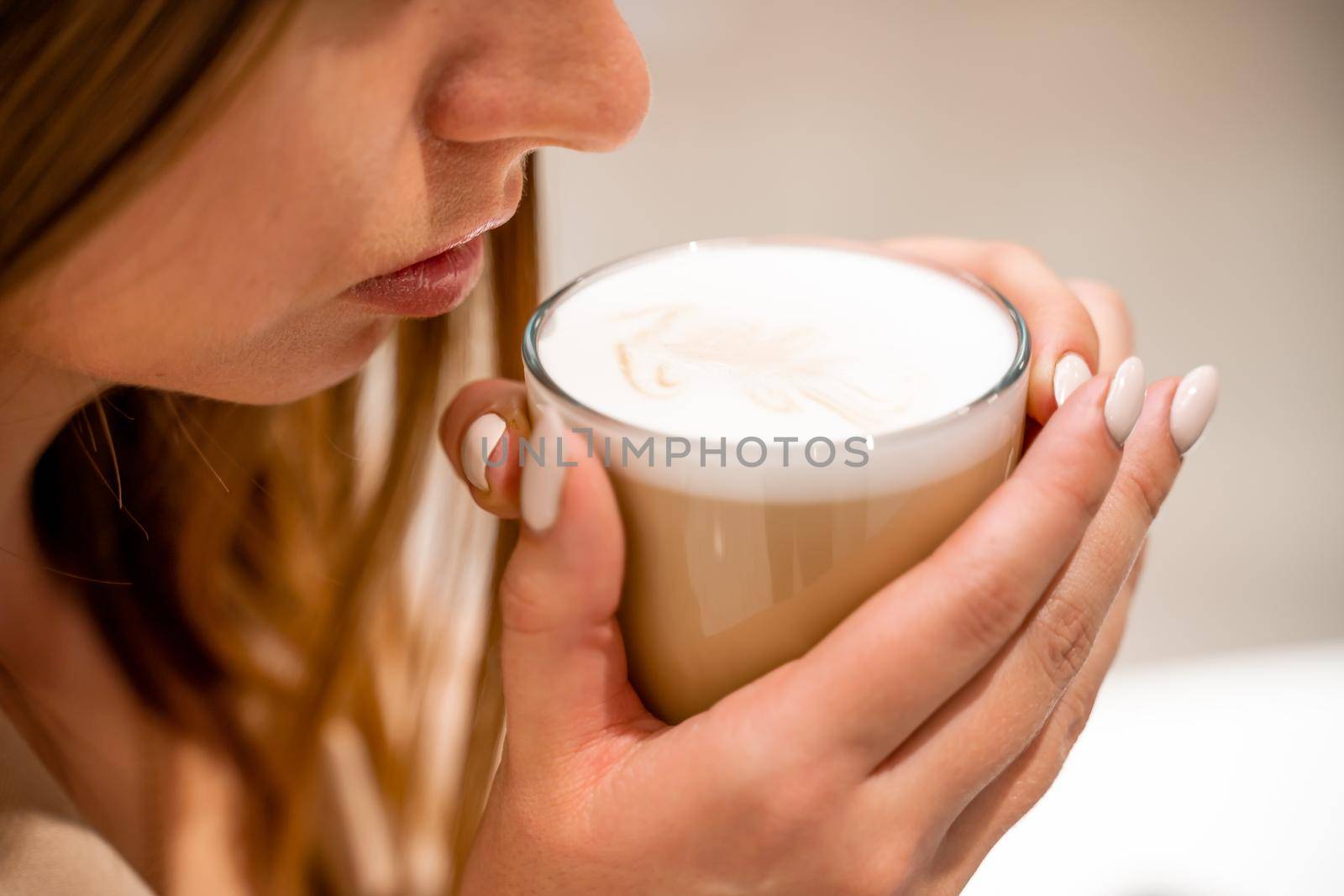 Close-up of beautiful female hands holding a large white cup of cappuccino. A woman is sitting in a cafe. by Matiunina