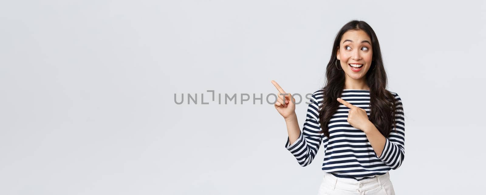 Lifestyle, people emotions concept. Excited good-looking asian girl smiling pleased as found excellent product, pointing fingers left at advertisement and looking satisfied, recommend promo.