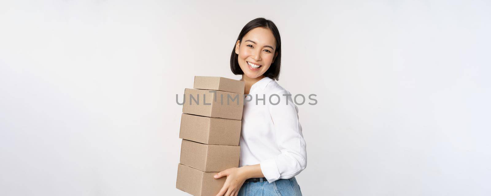 Portrait of young asian woman holding boxes, carry delivery goods. Korean female entrepreneur assemble order, standing voer white background.