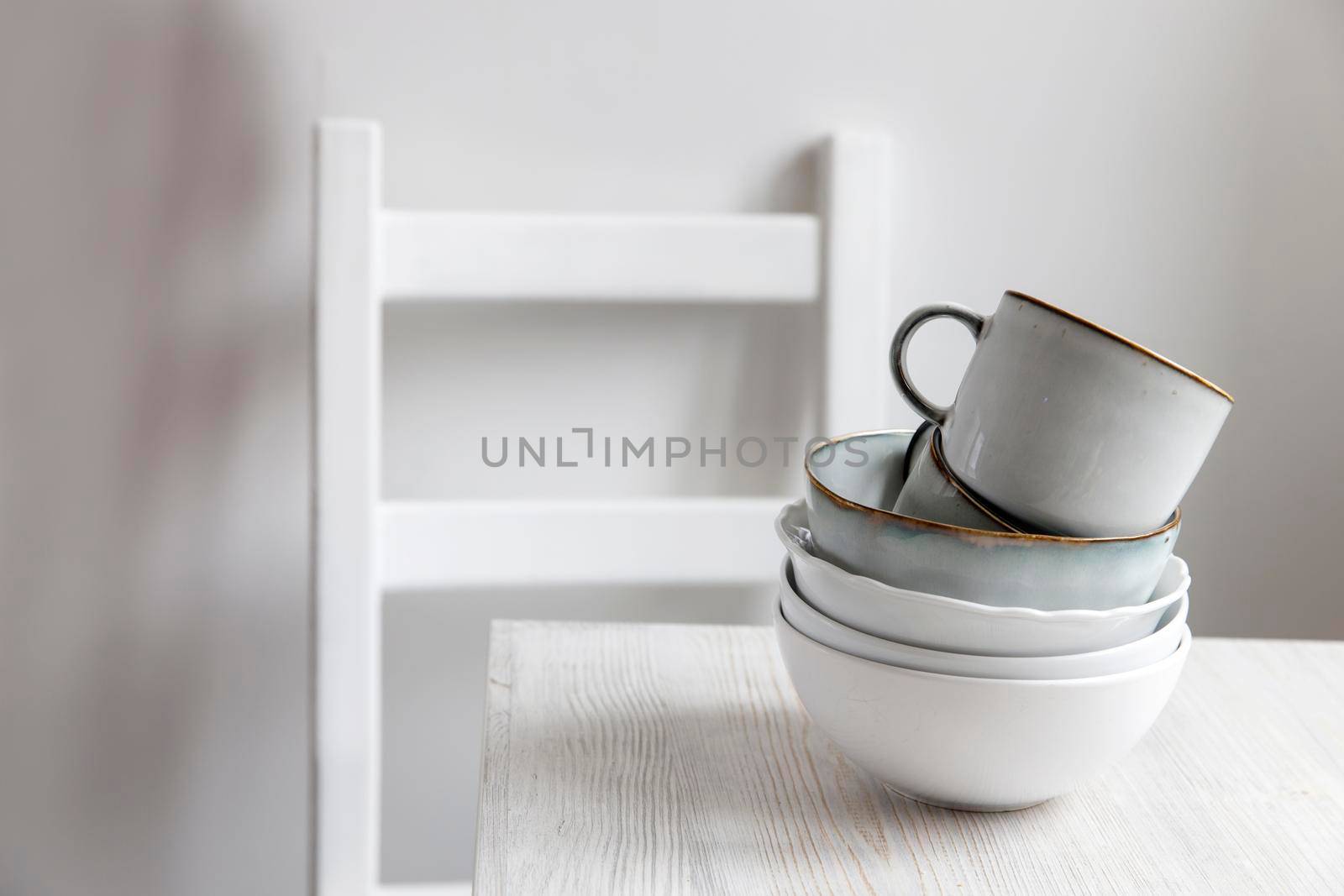 A pyramid of white bowls, plates and cups of different sizes and colors on a beige table in the kitchen. Scandinavian style. Place for your text. Copy space