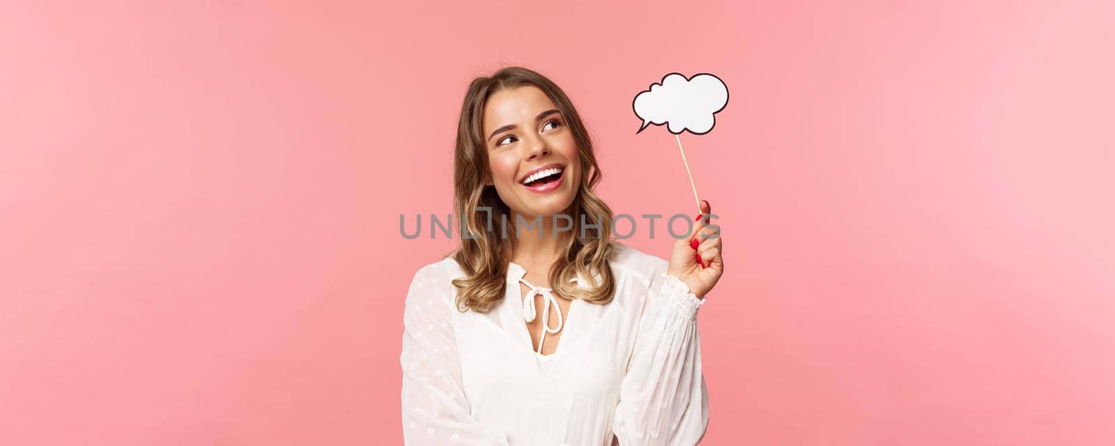 Spring, happiness and celebration concept. Dreamy and lovely blond girl daydreaming, saying something, holding comment cloud stick near mouth as if talking, look away daydreaming by Benzoix