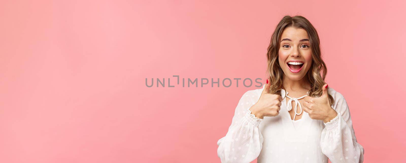 Close-up portrait of satisfied and impressed blond girl leave positive feedback about cafe or place she was attending, show thumbs-up in like and approval, smiling pleased, pink background.