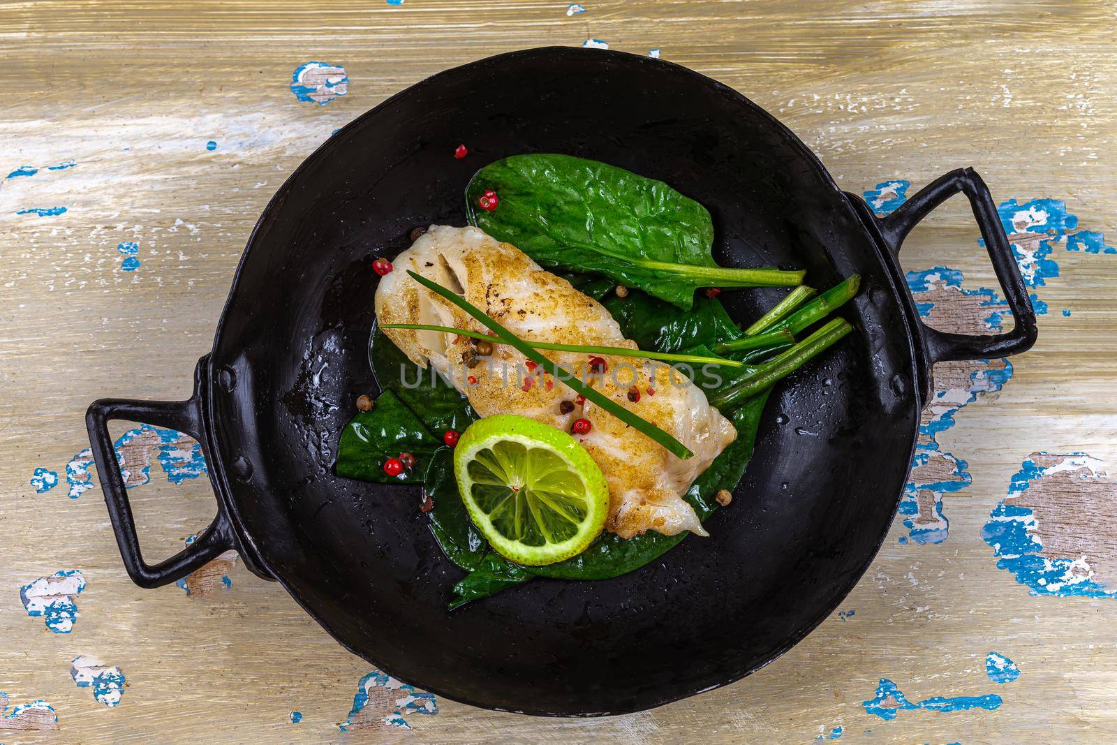 Cod back at the end of cooking in an old black dish-Top view.