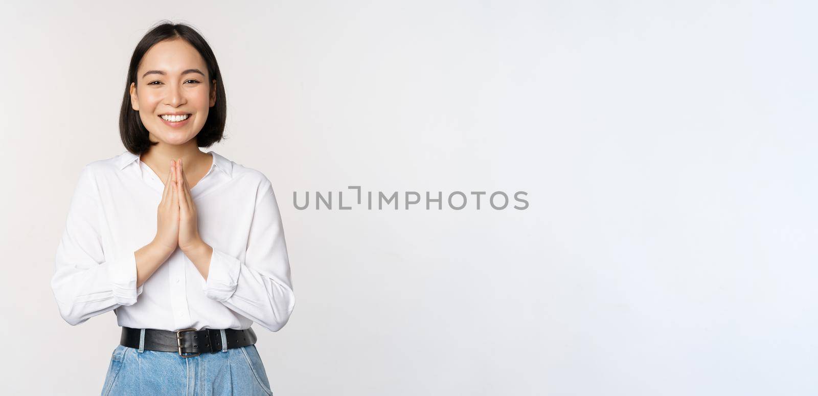 Portrait of happy asian girl laughing and smiling, showing thank you, namaste gesture, grateful for smth, standing over white background.