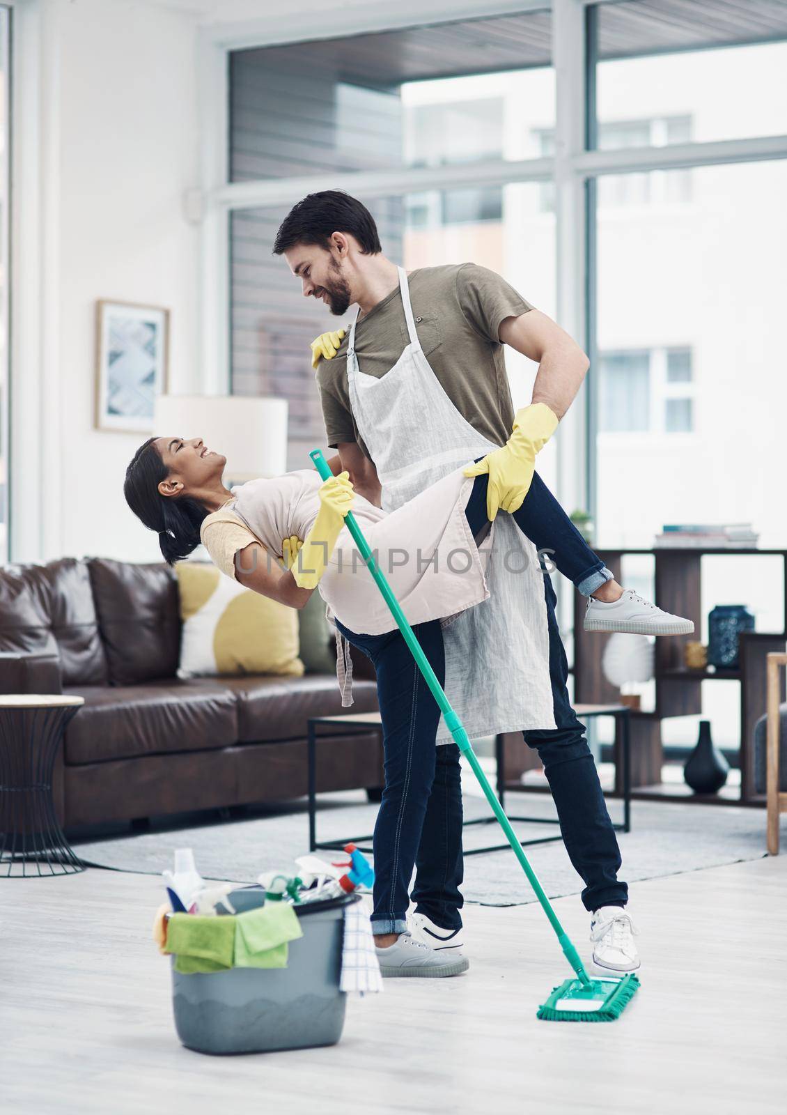 Romance changes everything. Shot of a happy young couple dancing while mopping the floor at home. by YuriArcurs