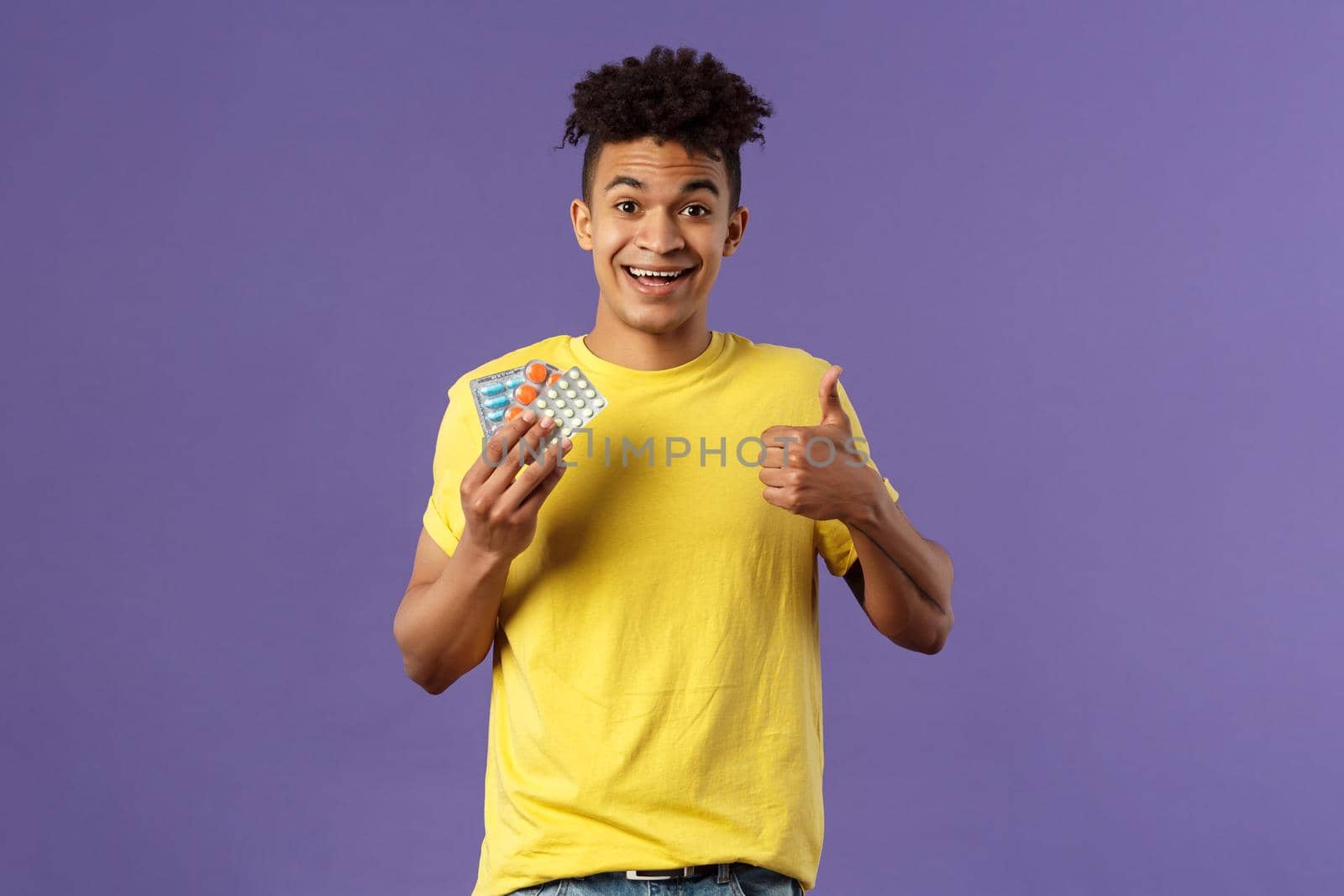 Health, influenza, covid-19 concept. Portrait of young healthy man got better, show thumbs-up holding drugs, taking pills to feel better after catching cold, being sick, purple background by Benzoix