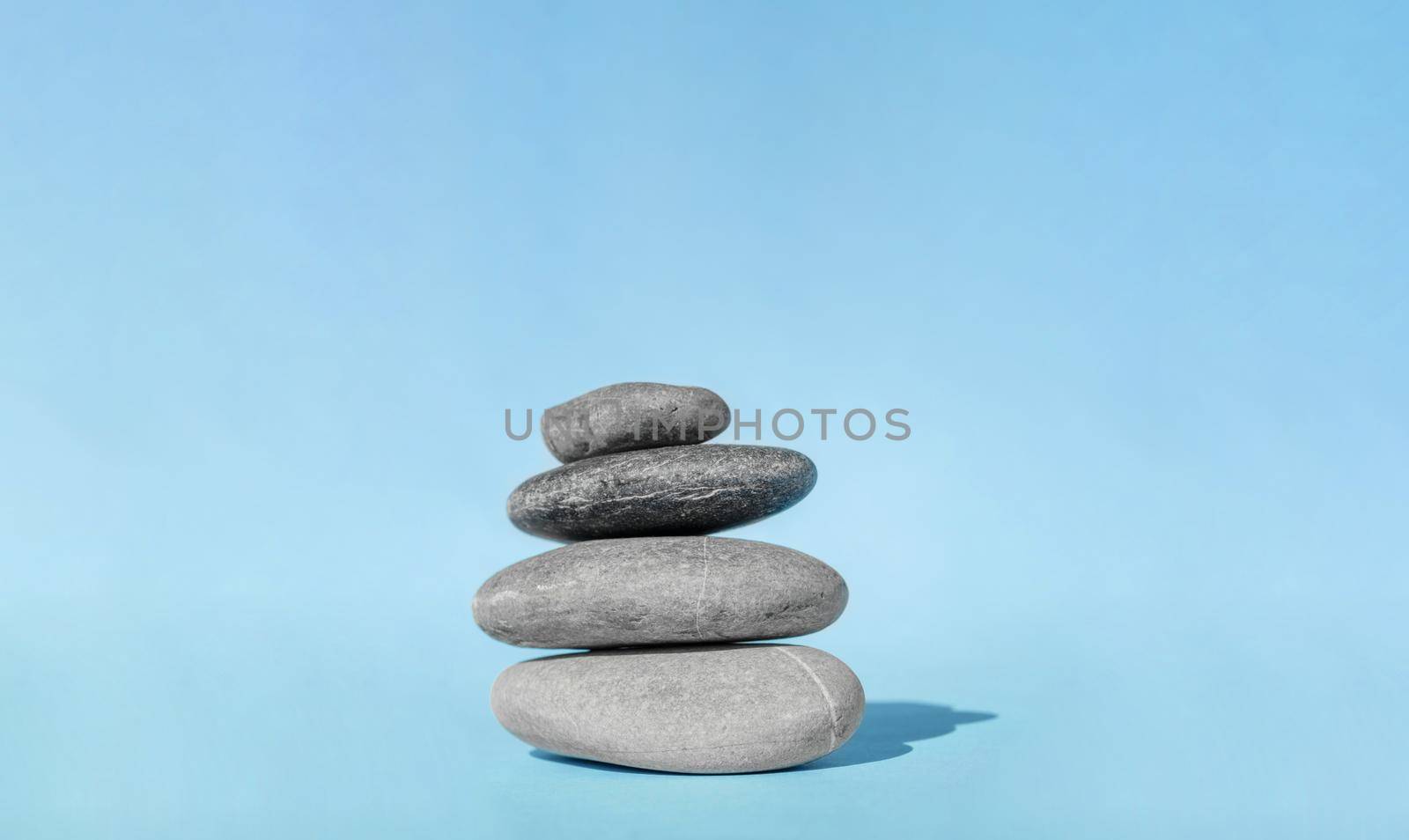 Balanced pebble stones for spa treatments on blue background. The balancing cairn - symbol of harmony, tranquility and relaxation, concept of meditation. Stack of spa hot stones.