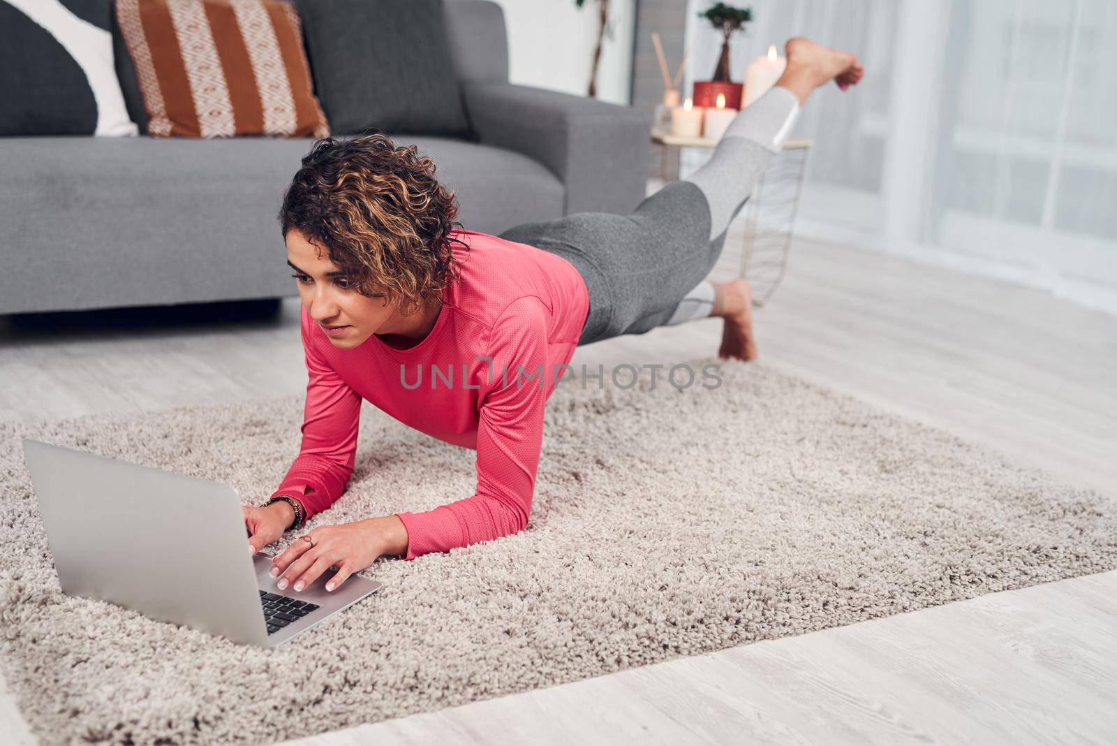 Full length shot of an attractive young woman multitasking and doing pilates while using a laptop in the living room.