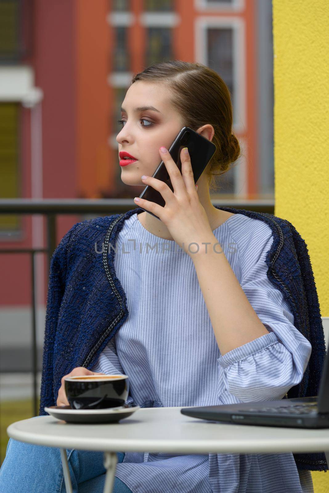 Charming happy woman student communicates by phone and use laptop computer to prepare for the course work. Concept of working outdoors