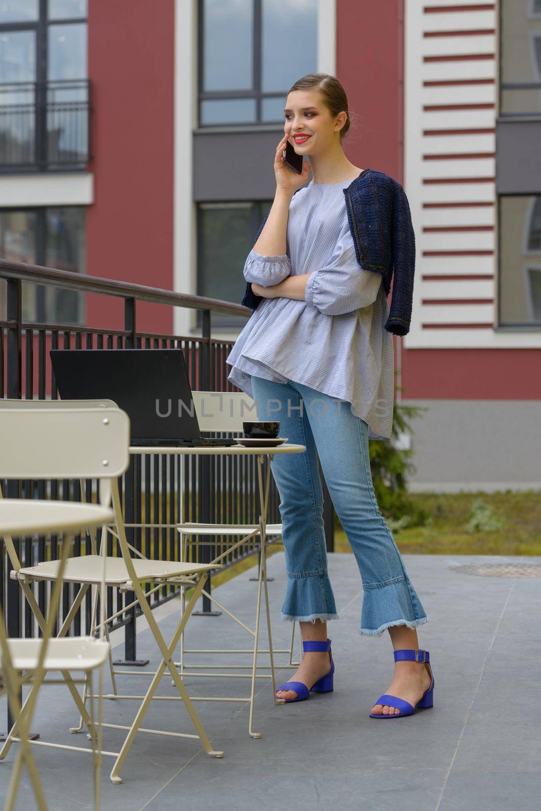 Charming happy woman student communicates by phone and use laptop computer to prepare for the course work. Concept of working outdoors