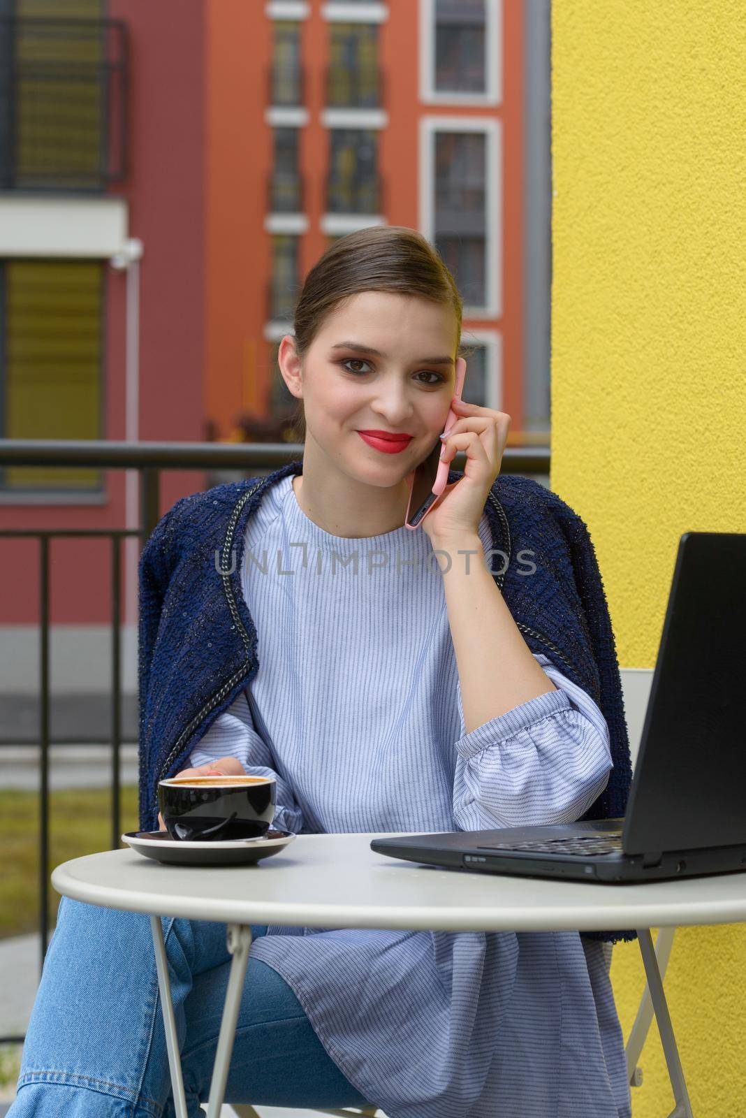 Charming happy woman student communicates by phone and use laptop computer to prepare for the course work. Concept of working outdoors