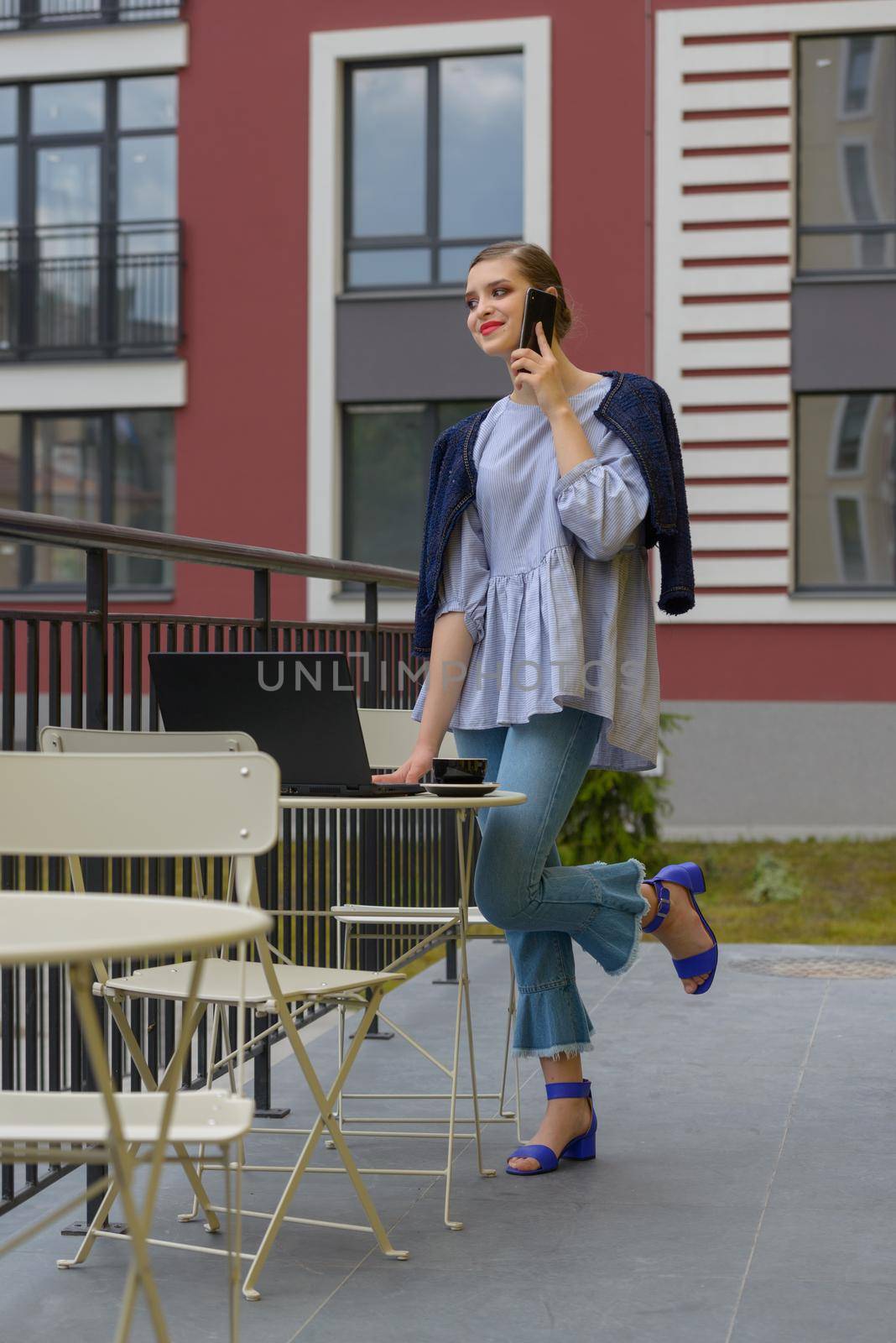 Charming happy woman student communicates by phone and use laptop computer to prepare for the course work. by Ashtray25