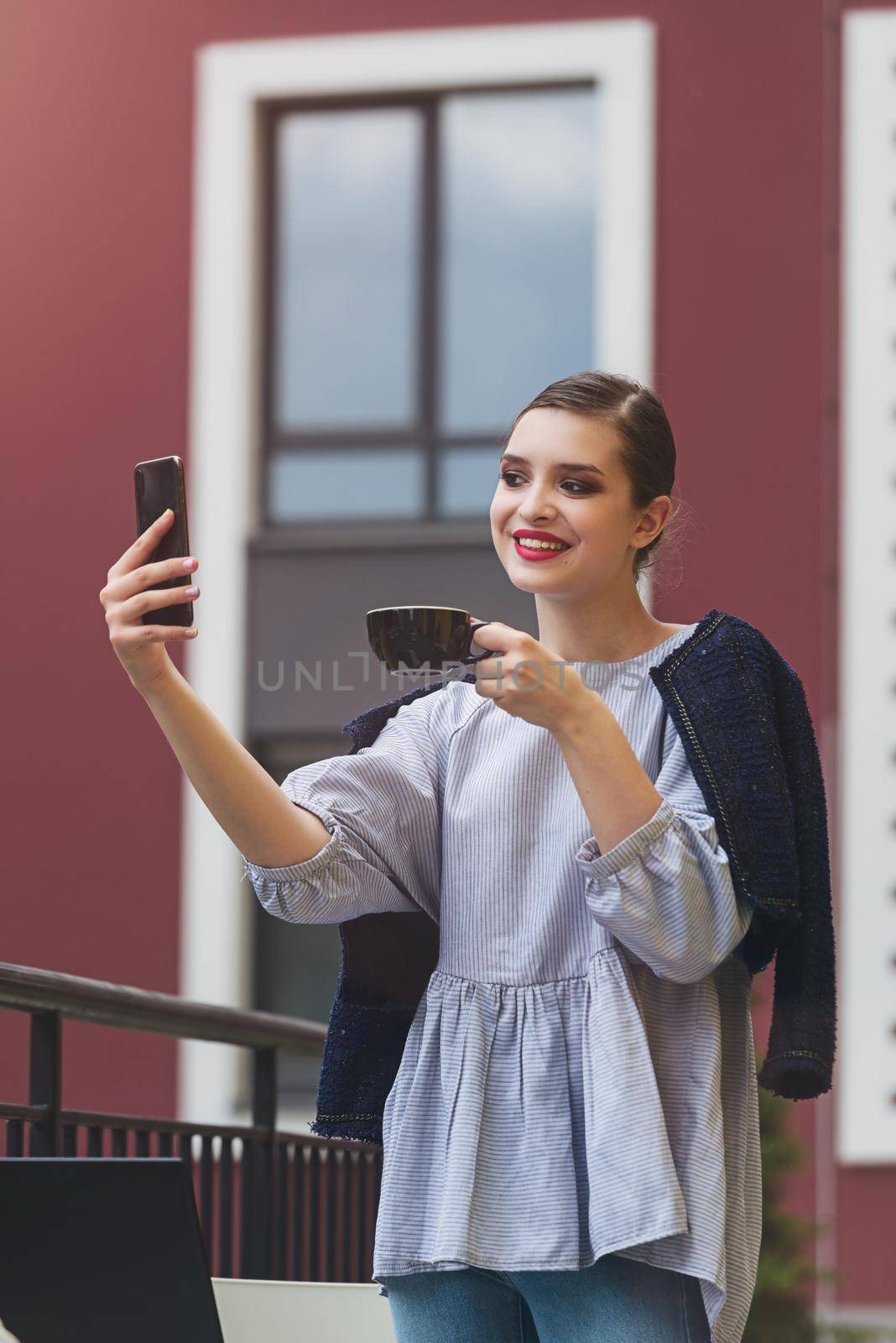 Charming happy woman student communicates by phone and use laptop computer to prepare for the course work. Concept of working outdoors