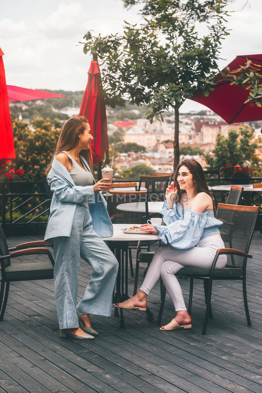 two young women friends at a cafe having breakfast, discussing the news, laughing. females in the cafe drink cocktails. by Ashtray25