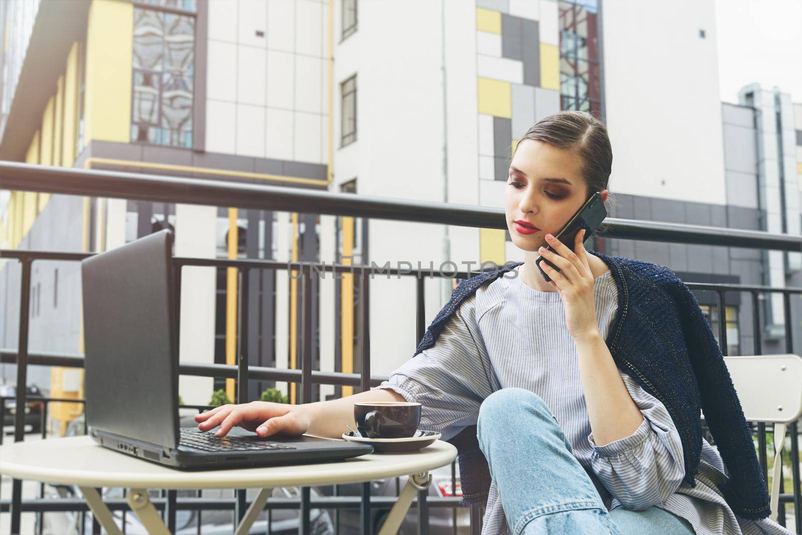 Charming happy woman student communicates by phone and use laptop computer to prepare for the course work. by Ashtray25