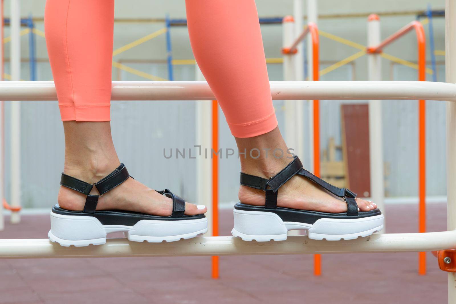 Sexy woman's sunburnt legs wearing black sandals and peach leggings, outdoors. white pedicure