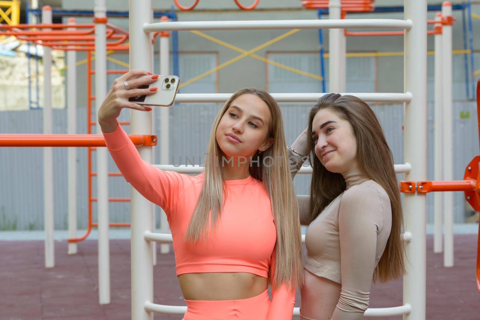 Two sporty young sexy women posing while taking selphy on the summer playground. Healthy lifestyle concept.