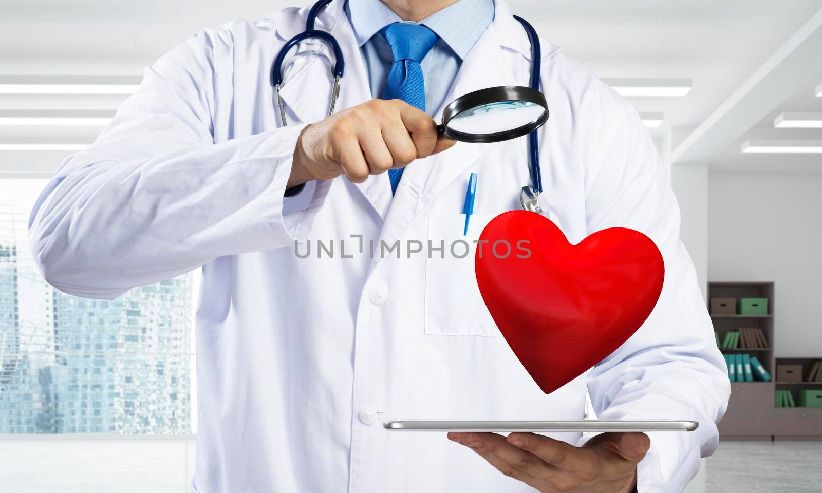 Conceptual image of professional doctor in white medical uniform is studying red heart symbol through magnifier while standing inside bright clinical building.