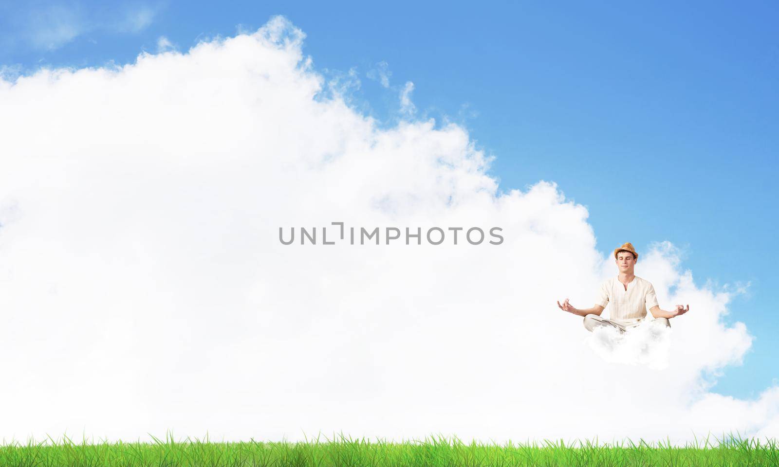 Young man keeping eyes closed and looking concentrated while meditating on cloud in the air with bright and beautiful landscape on background.