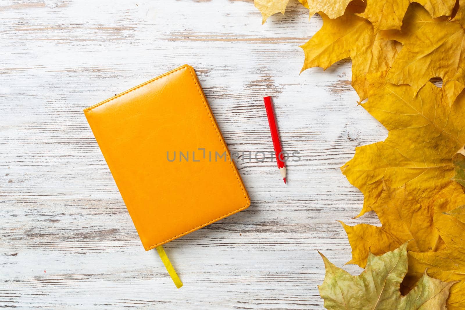 Notebook and pen lies on vintage wooden desk with bright foliage. Flat lay composition with autumn leaves on white wooden surface. Day planning and relaxation. Blank notepaper with copy space