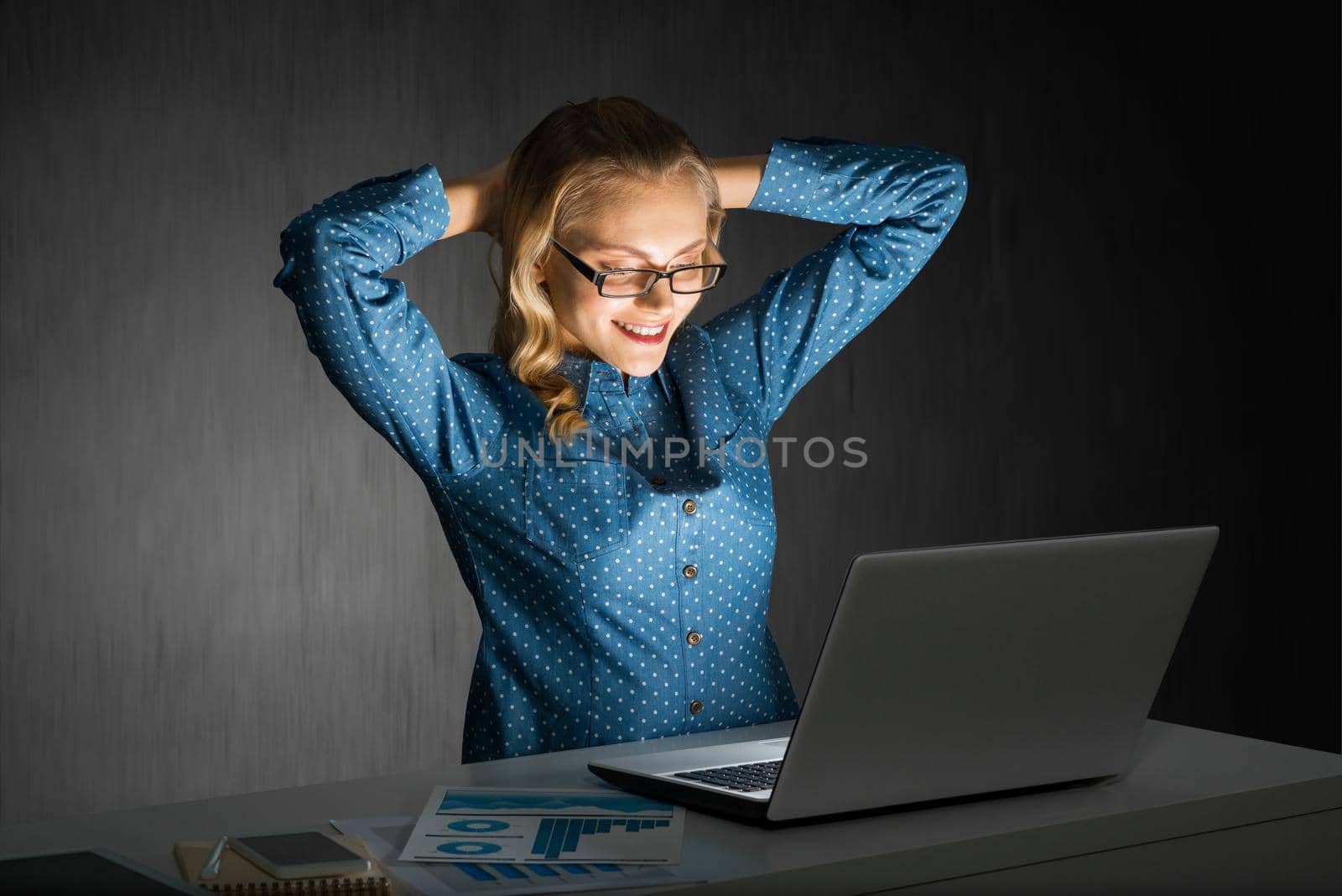 Attractive blonde working on laptop in dark office. Mixed media by adam121