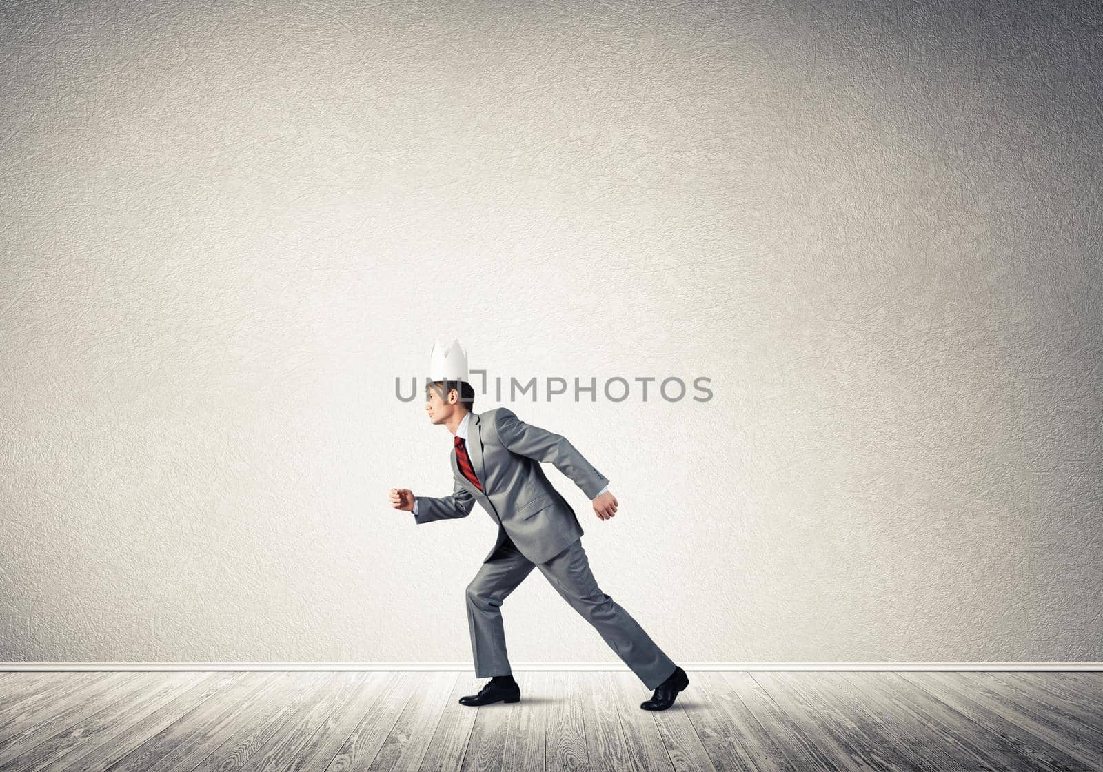 Young handsome businessman wearing white paper crown running in a hurry