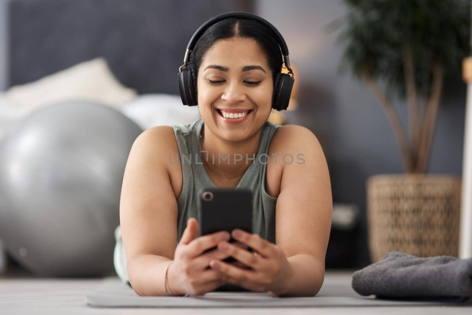 Shot of a sporty young woman wearing headphones and using a cellphone while exercising at home.