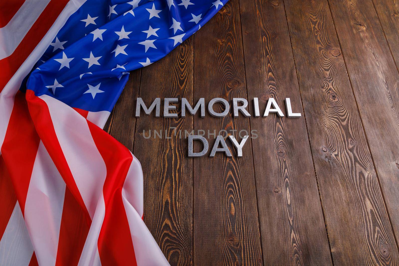 the words memorial day laid with silver metal letters on wooden board surface with crumpled usa flag.