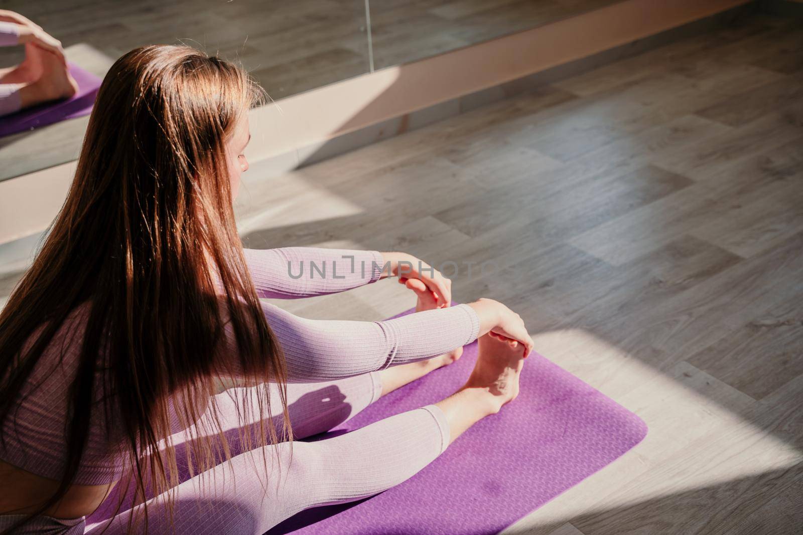 View from above. A beautiful young woman in pink sportswear is engaged in yoga, sports in the hall on a purple rug. Yoga, sport and healthy concept