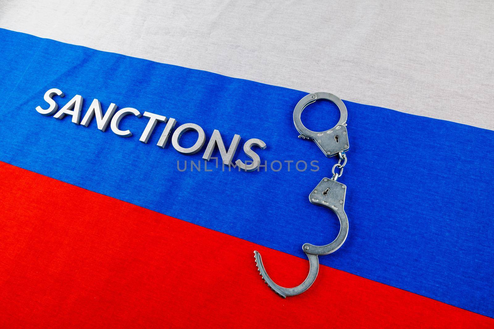 the word sanctions laid with silver metal letters on russian tricolor flag near handcuffs over it in directly above view
