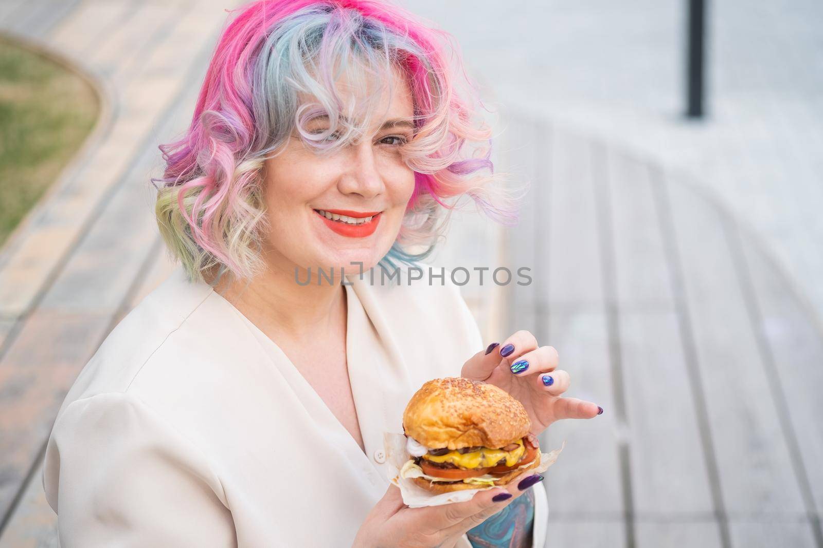 Caucasian woman with curly colored hair eating burger. Bad eating habits and love of fast food by mrwed54