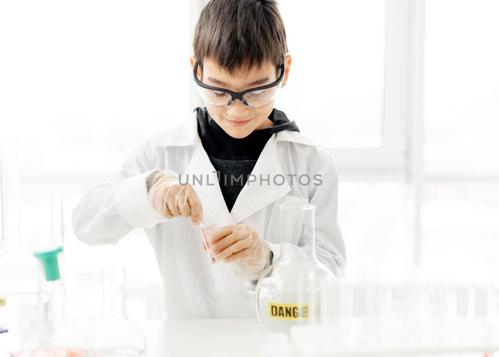 School boy wearing protection glasses doing chemistry experiment in elementary science class. Pupil with equipment tubes in lab
