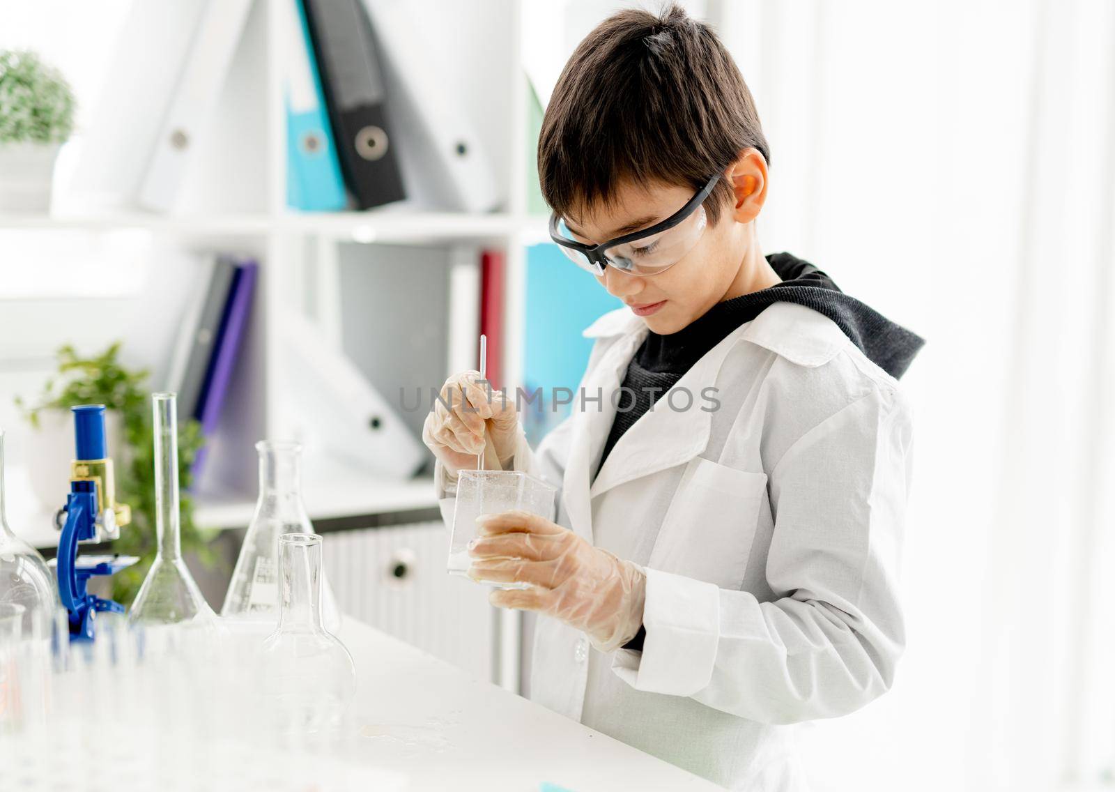 School boy wearing protection glasses doing chemistry experiment in elementary science class. Clever pupil with tubes in lab during test