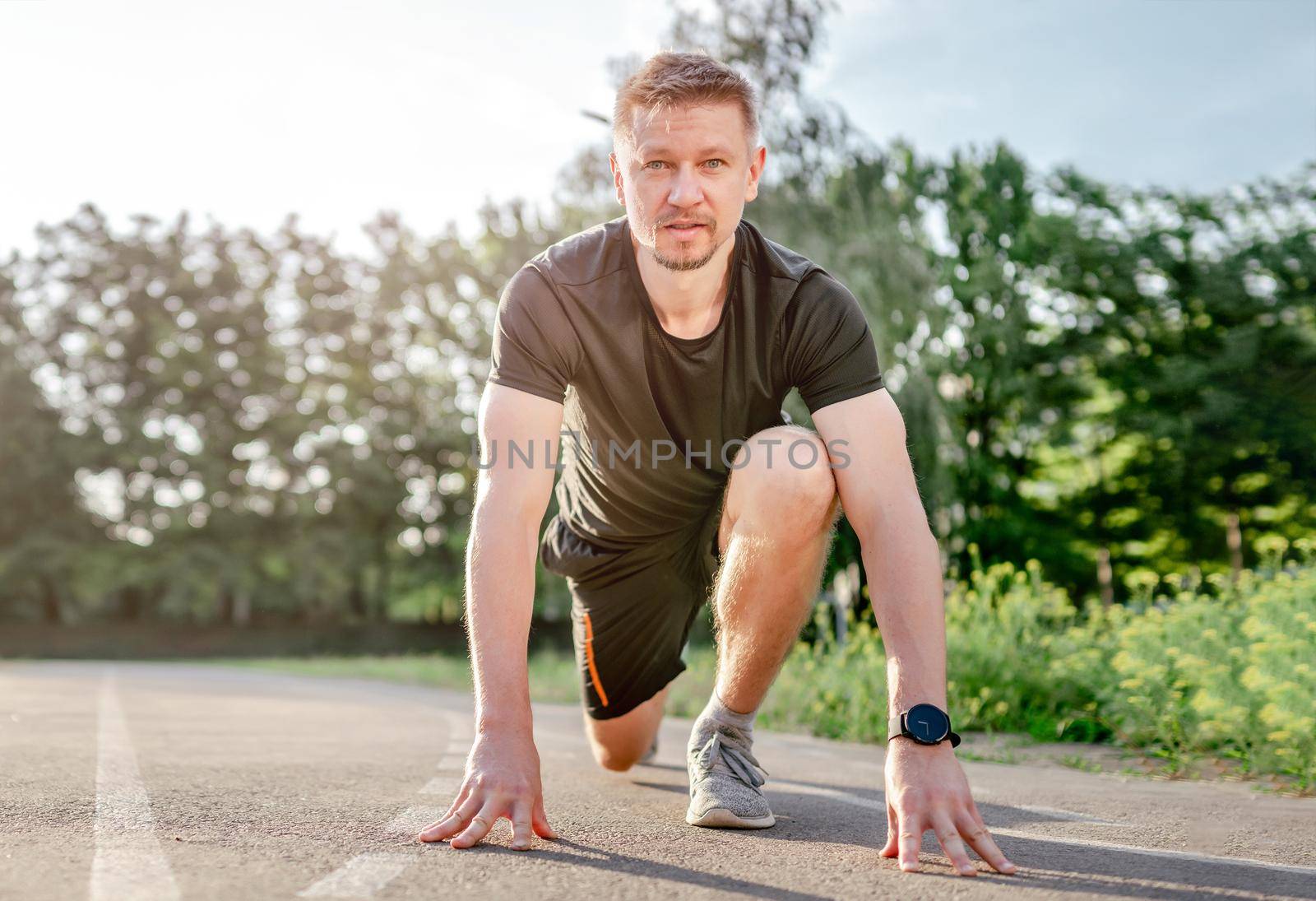 Man guy going to start running at the stadium and standing in the pose outdoors in summertime. Male person during workout outside. Sportsman exercising