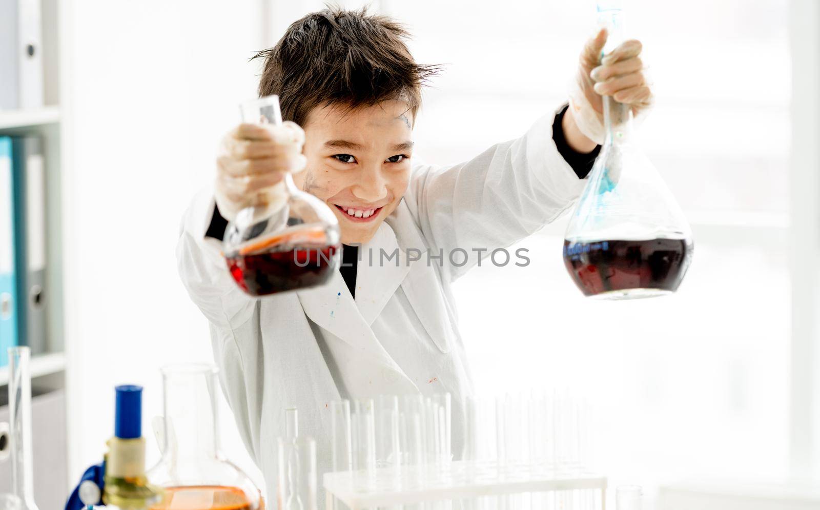 School boy holding two bottles with chemical liquids during chemistry experiment in elementary science class. Clever pupil kid in lab