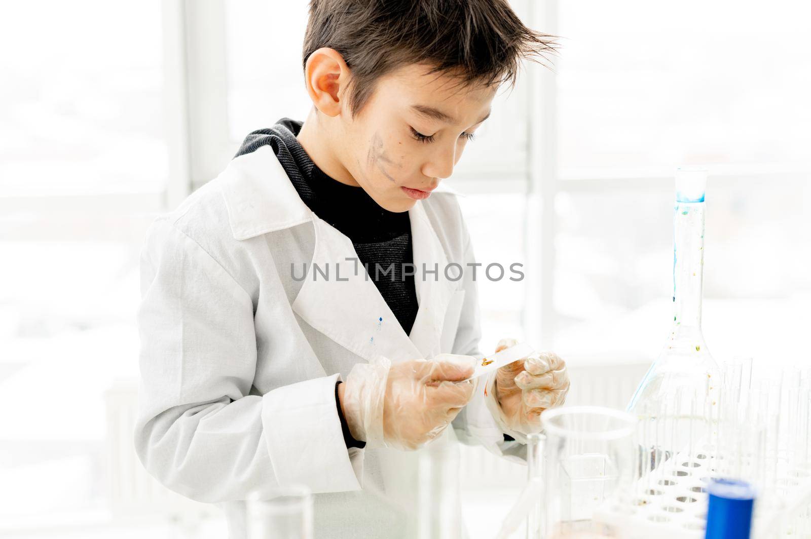 School boy checking test results during chemistry experiment in elementary science class. Clever pupil in lab