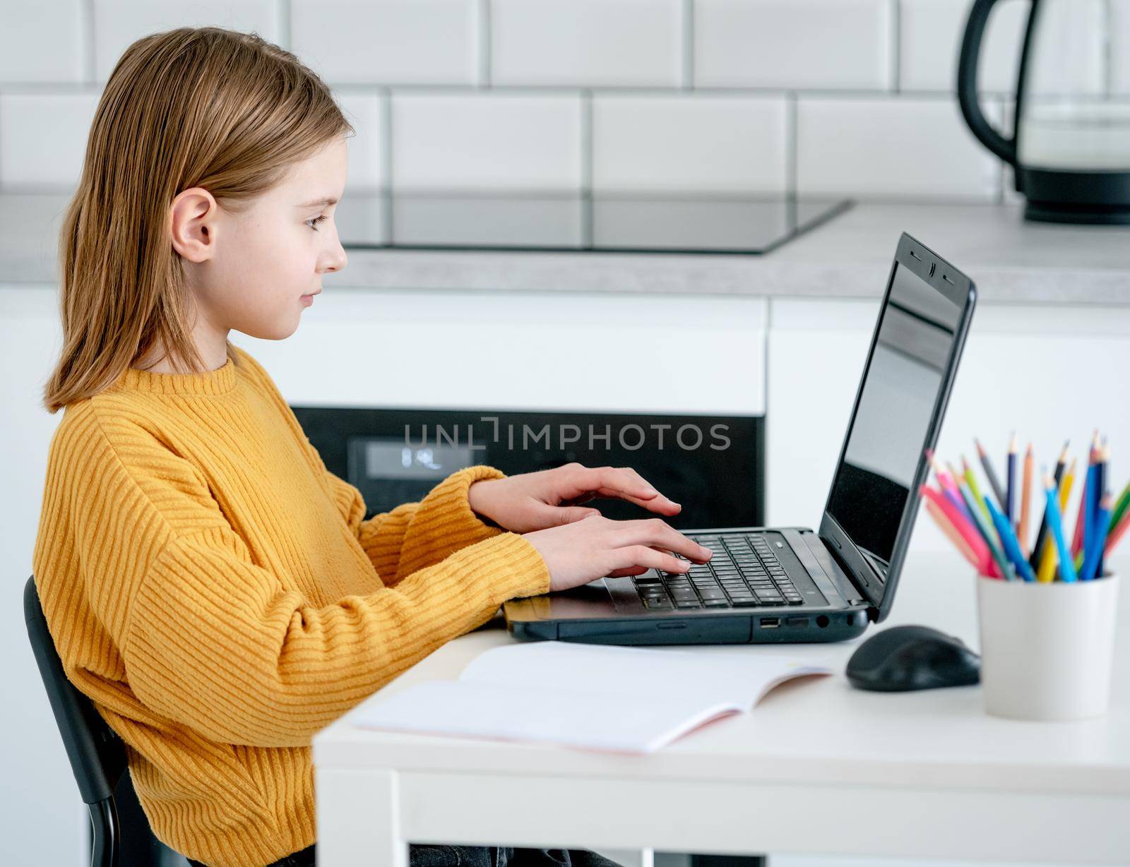 Preteen girl with laptop studying during remote lesson by internet. Pretty schoolgirl learning with pc and having class online with new technologies at covid time