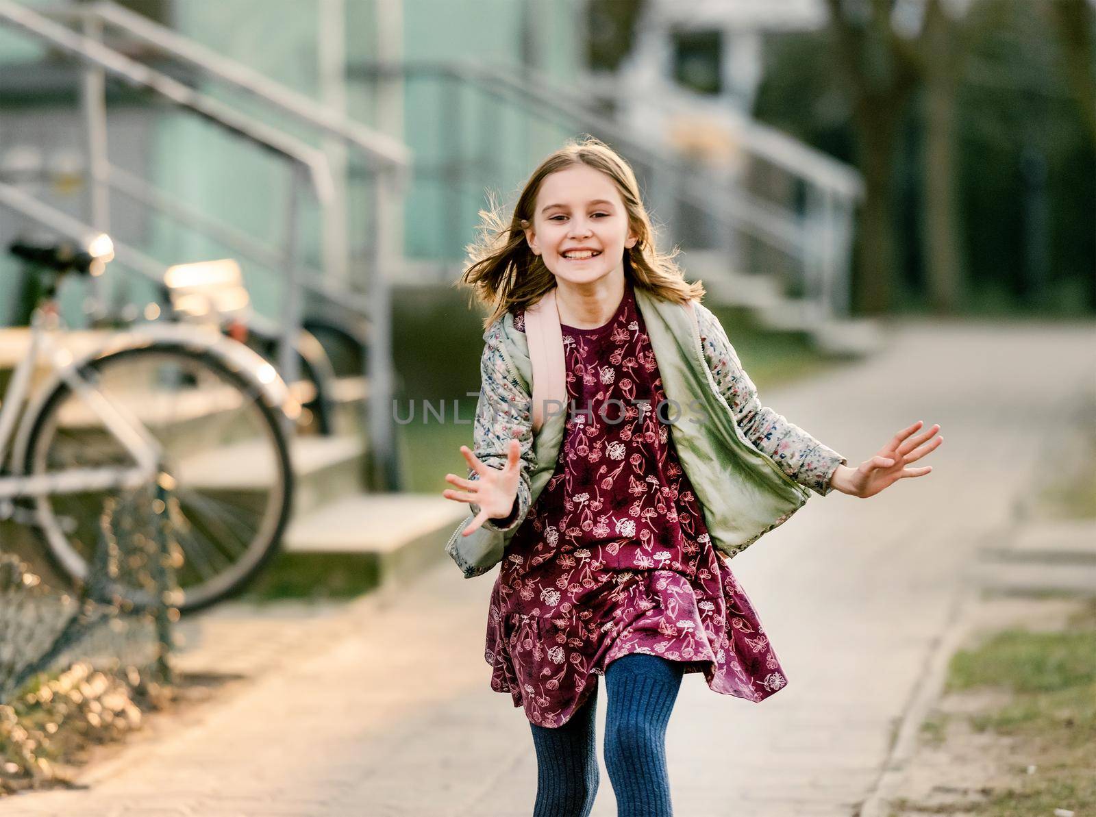 Preteen girl child with backpack at street running, smiling and looking at camera. Pretty schoolgirl going home after class