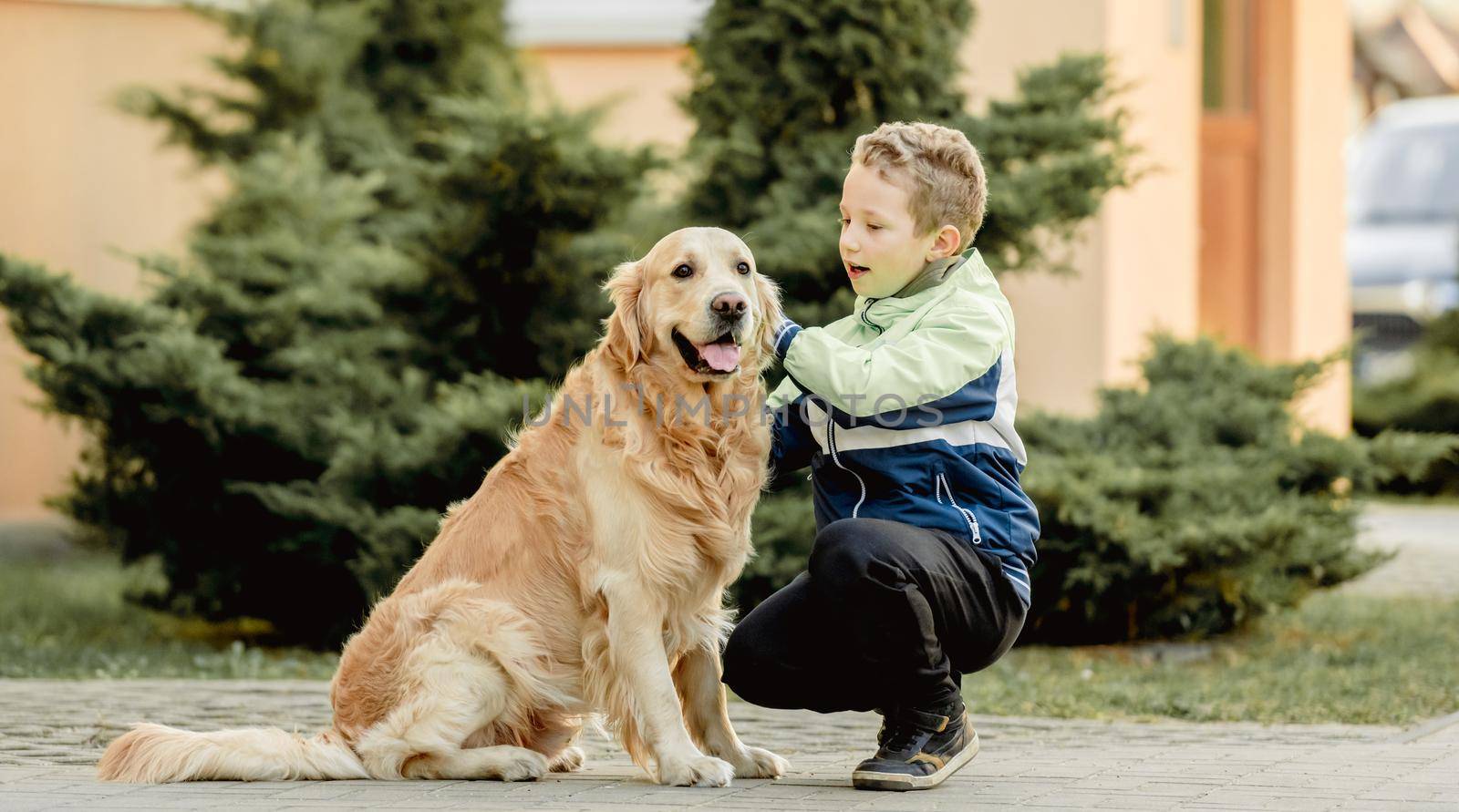 Preteen boy with golden retriever dog sitting outdoors. Child kid with doggy pet at street