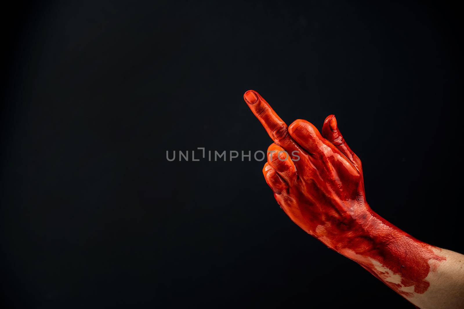 Female hand stained with blood shows the middle finger on a black background