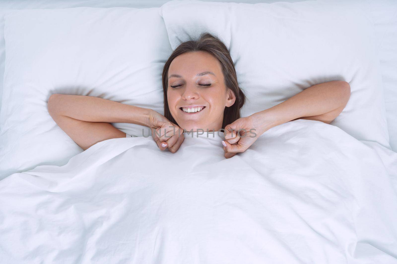 Good morning. Top view of beautiful young woman wakening up happy in the white bed. Day off work. High quality photo