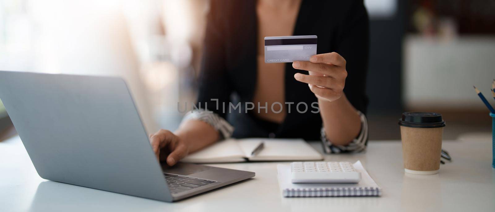 Young woman holding credit card and using laptop computer. Businesswoman working at home. Online shopping, e-commerce, internet banking, spending money, working from home concept.