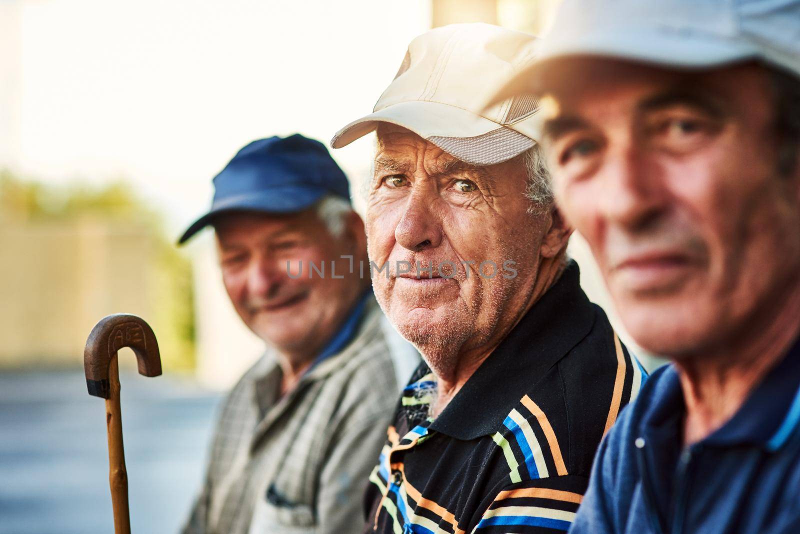 Portrait of a group of cheerful senior men sitting together while looking into the camera outside.