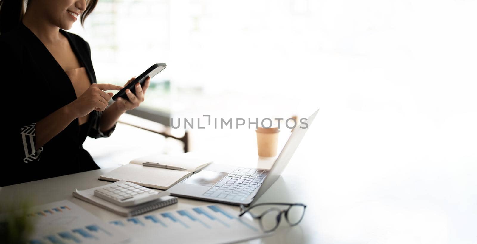 Asian woman holding smart phone while using calculator and laptop for business financial accounting calculate money bank loan rent payments manage expenses finances taxes doing paperwork concept, close up