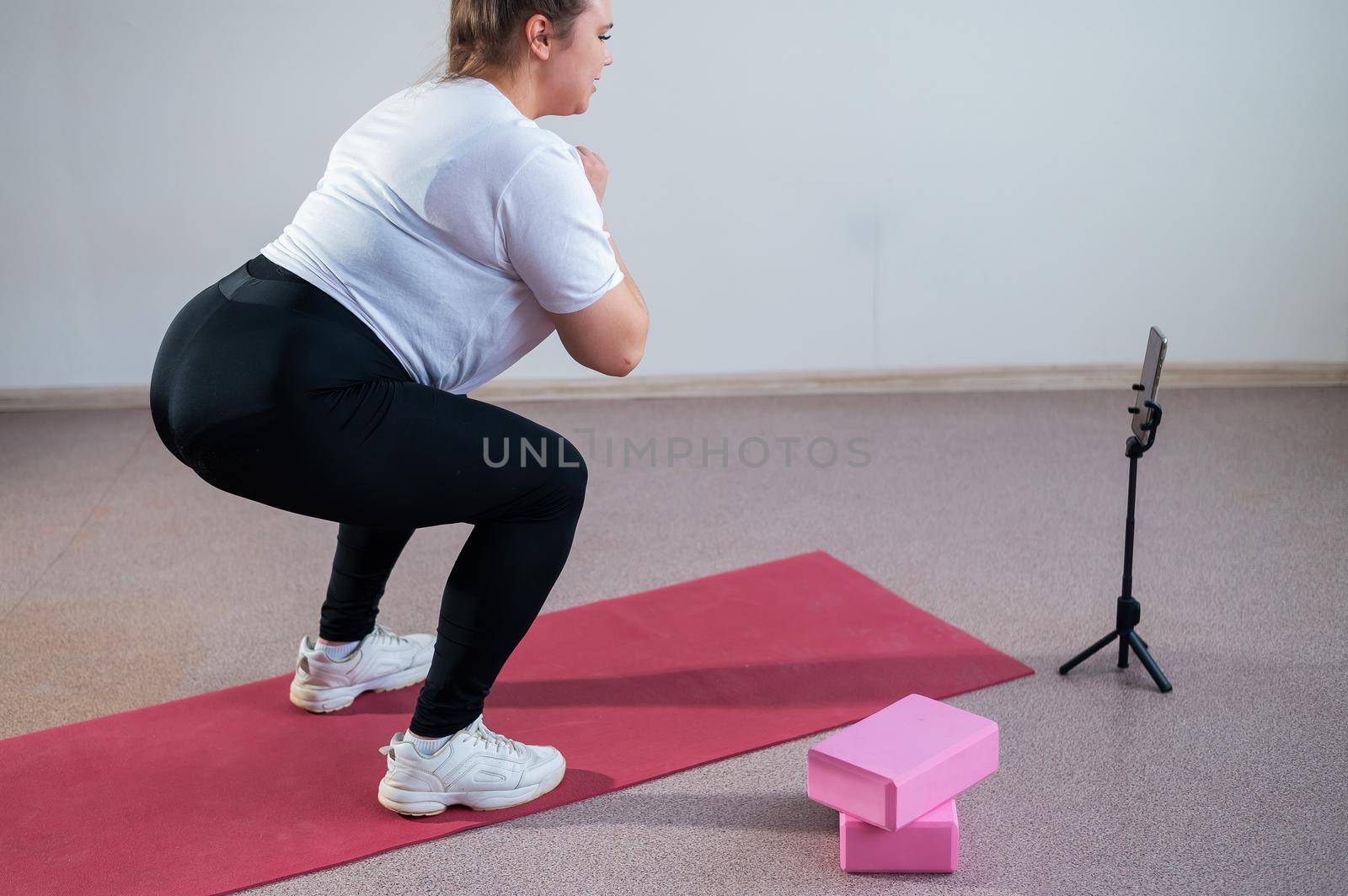 A chubby young woman is watching an online fitness lesson on a mobile phone. Distance sports training by mrwed54